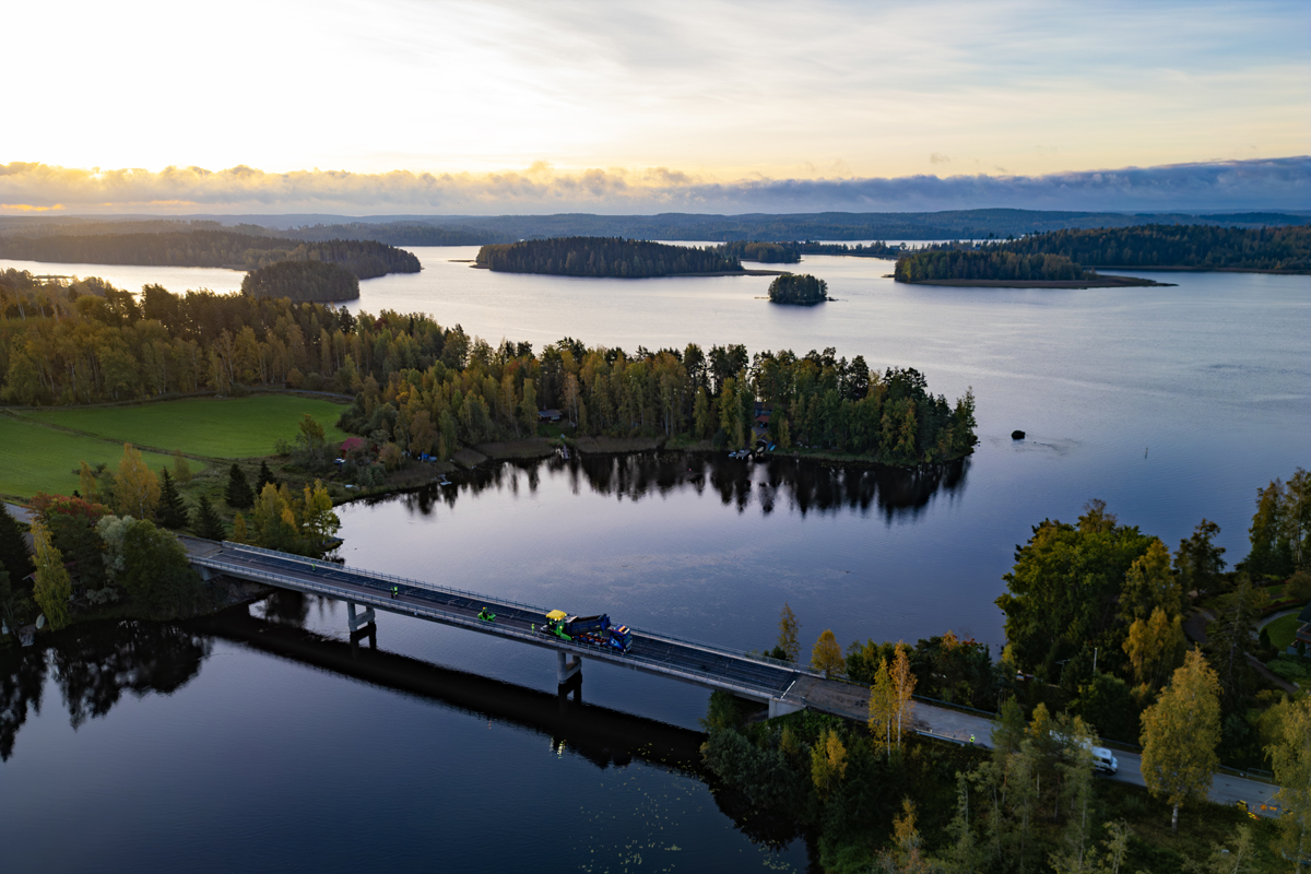 Asfalttikallion työkoneita sillalla kauniissa saaristomaisemassa ylhäältä päin kuvattuna.